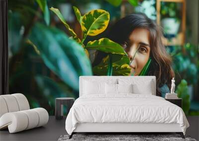 A woman is looking at a plant with her face covered by a leaf. Concept of curiosity and wonder as the woman explores the plant Wall mural