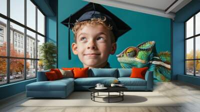 A young boy wearing a graduation cap looks at a chameleon beside him with a curious smile. Wall mural