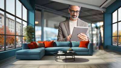 Busy mature older business man executive standing in office using digital tablet. Middle aged professional businessman corporate manager wearing suit and glasses holding tab working on finance project Wall mural