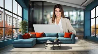 Busy mid aged business woman working in office using laptop writing. 40 years old female professional executive manager looking at computer, elearning, having hybrid meeting sitting at desk. Wall mural