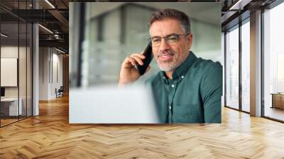 Busy older middle aged business man professional expert or entrepreneur making phone call speaking with client on cellphone using laptop computer. Work communication on smartphone in office. Wall mural