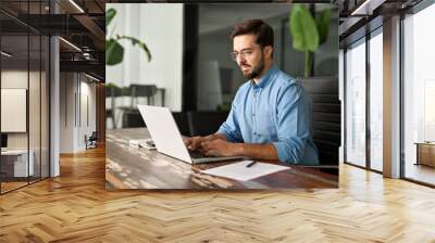 Busy professional business man executive, young male corporate worker, latin businessman wearing glasses typing on computer technology using laptop searching on web working at office workplace desk. Wall mural