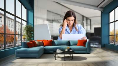 Busy professional mature business woman reading bad news in document at work. Worried serious middle aged businesswoman entrepreneur looking at paper bill sitting at desk in office. Wall mural