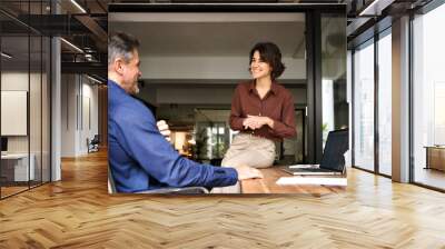 Candid photo of two happy hispanic professional business man and woman having friendly conversation at work. Executives team business people working talking at workplace in corporate office. Wall mural