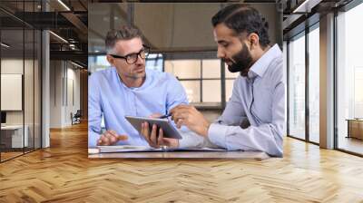 Caucasian and Indian businessmen ceo negotiating at table meeting using holding tablet device computer. Multiethnic executive team discussing financial report planning sitting at table in office. Wall mural