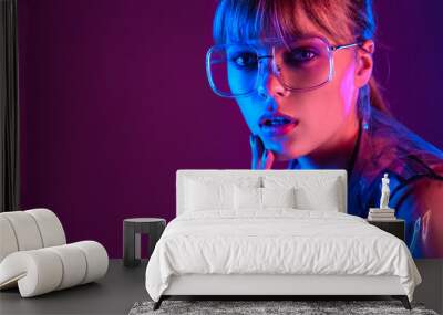 Chic attractive fashion sexy young woman girl beauty face wear stylish trendy transparent raincoat eyewear glasses look at camera in neon light purple blue studio background, portrait, copy space. Wall mural