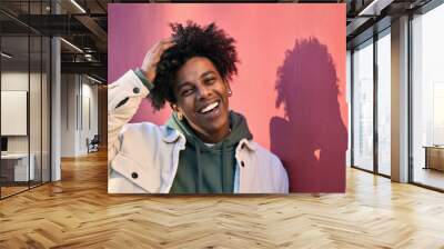 Close up portrait photo of young happy African American cool hipster teen guy face laughing on red city wall lit with sunlight. Smiling cool rebel gen z teenager model standing outdoors. Headshot. Wall mural