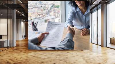 Closeup of Indian latin ceo holding employment contract job offer hiring welcoming female African American newcomer worker manager shaking hands in contemporary office. Human resources concept. Wall mural