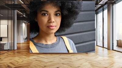 Closeup of young beautiful African American girl of 20s standing on black wall background. Headshot of stylish serious black teenage student with curly hair looking at camera. Wall mural