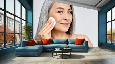 Closeup portrait isolated on white of beautiful middle age Asian 50 woman doing everyday routine removing makeup with cotton pad enjoying anti age healthy perfect products skin. Beauty care ads. Wall mural