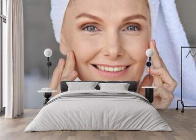 Closeup portrait of happy smiling gorgeous middle aged woman wearing bathrobe and white towel with perfect complexion touching face looking at camera in bathroom. Advertising of skincare cosmetology. Wall mural