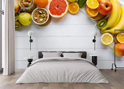 Colorful fresh summer fruits banana orange apple kiwi grapefruit and  granola cashew on white wooden background, healthy organic super food on table, nutrition for health care, top view, copy space Wall mural