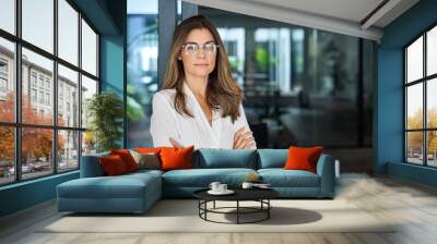 Confident 45 year old Latin professional mid aged business woman corporate leader, mature female executive manager wearing eyeglasses standing in office arms crossed looking at camera, portrait. Wall mural