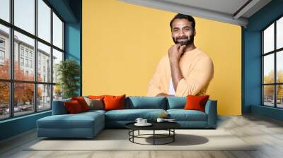 Confident rich bearded indian man standing isolated on yellow background. Happy handsome ethnic guy wearing shirt looking at camera advertising products thinking on offer for portrait. Wall mural