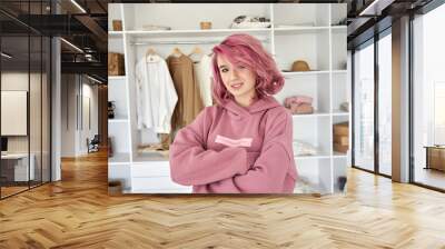 Cool confident stylish hipster gen z teen girl fashion designer, stylist with pink hair piercing wear hoodie looking at camera stand arms crossed in front of modern clothes wardrobe closet, portrait. Wall mural