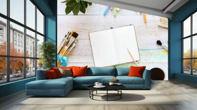 Creative art designer workplace, artistic mock up, blank notebook for sketches with pencil on it, set of paintbrushes and cup of coffee on white wooden table, top view, copy space, flat lay style Wall mural