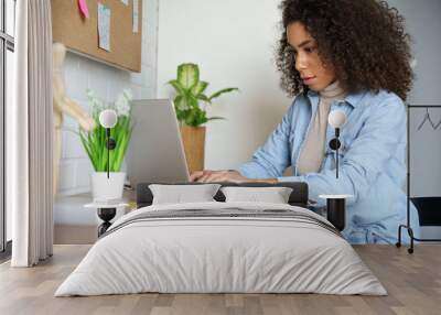 Focused young african american teen girl college student using laptop computer typing studying working online. Serious mixed race millennial woman doing internet research sitting at home office desk. Wall mural