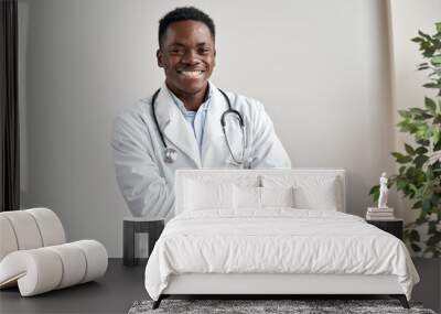 Happy african male doctor wearing white coat, stethoscope looking at camera standing with arms crossed in medical office. Smiling black man professional therapist physician posing at wor, portrait. Wall mural