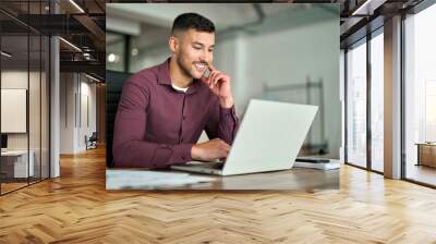 Happy busy Latin business man employee or manager working on digital technology project sitting at desk. Young smiling professional businessman entrepreneur using computer laptop in office. Wall mural