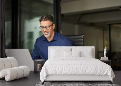 Happy busy older professional businessman entrepreneur using laptop holding bill corporate document in office. 50 years old man executive manager or business owner reading paper working on computer Wall mural