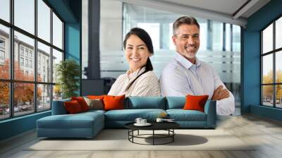 Happy confident professional mature Latin business man and Asian business woman corporate leaders managers standing in office, two diverse executives team posing arms crossed, vertical portrait. Wall mural