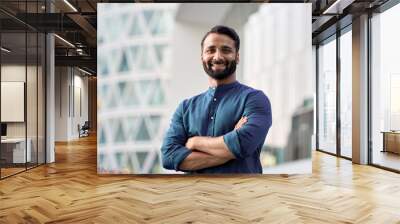 Happy confident wealthy young indian business man leader, successful eastern professional businessman crossing arms looking at camera posing outdoors in urban big city for close up headshot portrait. Wall mural