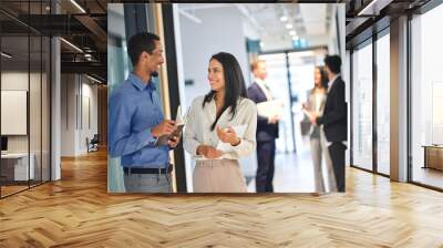 Happy diverse colleagues standing in office hallway, laughing and talking. Cheerful international business team people two Latin and African American coworkers executives having fun, authentic shot. Wall mural