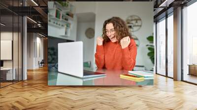 Happy girl student winner looking at laptop receiving good news in email celebrating achievement success. Excited woman winning online, getting new approved job opportunity using computer at home. Wall mural