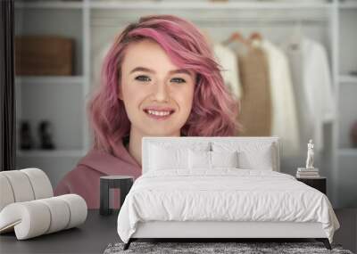 Happy hipster gen z teen girl fashion designer, stylist with pink hair and piercing wearing hoodie looking at camera in front of modern clothes wardrobe closet, face head shot close up portrait. Wall mural