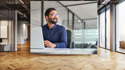 Happy Indian business man ceo executive looking away working on laptop. Smiling professional company manager or employee thinking of future financial success and growth at work in office. Copy space. Wall mural