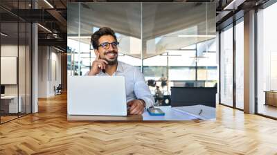 Happy Latin business man working at laptop in office looking away. Happy young businessman professional using computer sitting at desk thinking of corporate technology ai solutions. Copy space Wall mural