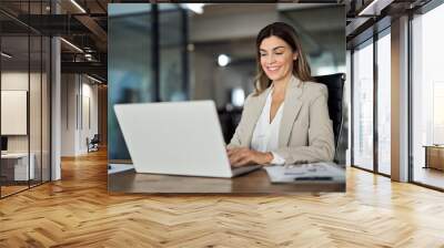 Happy mature business woman entrepreneur in office using laptop at work, smiling professional middle aged 40 years old female company executive wearing suit working on computer at workplace. Wall mural