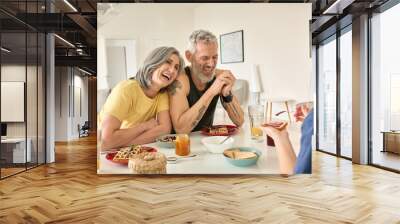 Happy mature family couple having breakfast with teen daughter sit at kitchen table. Cheerful older mid age parents having fun talking, eating toasts and waffles enjoying morning meal together. Wall mural