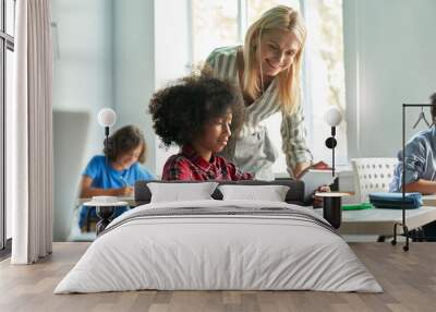 Happy mature female teacher educator helping African American junior school kid girl student using digital tablet computer education program app technology during elementary class lesson in classroom. Wall mural