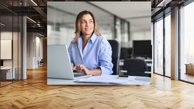 Happy mature middle aged professional business woman bank worker or hr manager, corporate executive looking away at work working on laptop computer in office thinking of business technology future. Wall mural