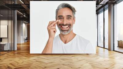 Happy middle aged 45 years old man applying facial anti age skincare cream on face isolated on white background. Smiling mature handsome gray-haired male model advertising skin care product. Portrait. Wall mural