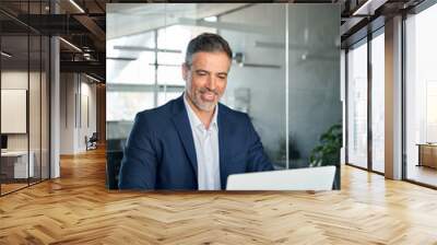 Happy middle aged business man ceo wearing blue suit sitting at desk in office using laptop. Mature businessman professional executive manager working on computer technology at workplace. Vertical Wall mural