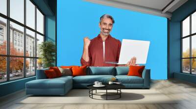 Happy middle aged business man entrepreneur, excited older professional businessman winner holding laptop celebrating online money profit, winning prize promotion standing isolated on blue background. Wall mural