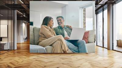 Happy middle aged couple using laptop computer relaxing on couch at home. Smiling mature man and woman talking having fun laughing with device sitting on sofa in sunny living room. Candid shot. Wall mural