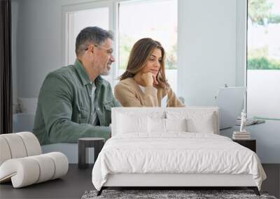 Happy middle aged mature man and woman paying bills online at home. Older senior couple using laptop computer checking insurance or financial invoice counting taxes sitting at table in living room. Wall mural