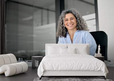 Happy middle aged senior curly business woman holding phone in office looking at camera. Smiling mature female entrepreneur, older professional worker using cellphone working at desk, portrait. Wall mural