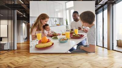 Happy multiracial diverse family couple with two children having morning breakfast at home together. Multiethnic young parents with mixed race kids eating pancakes meal sitting at kitchen table. Wall mural