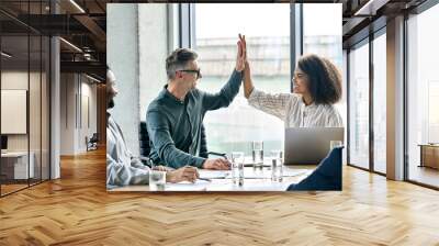 Happy multiracial professional ceo executive manager businessman and businesswoman colleagues giving highfive after successful project sit with international team at modern boardroom meeting table. Wall mural