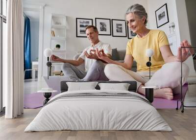 Happy old middle aged senior 50s couple learning to meditate at home watching live online tv yoga class tutorial on website looking at laptop computer doing virtual training fitness workout exercises. Wall mural