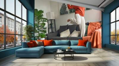 Happy pretty young woman wearing headphones dancing at home. Cheerful crazy funny girl listening music, moving, laughing, jumping on couch feeling joy standing on sofa in living room. Vertical Wall mural