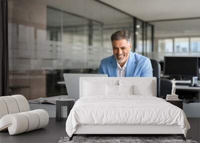 Happy senior 50 years old professional business man wearing suit using computer sitting at desk. Busy smiling middle aged businessman executive investor bank manager working on computer in office. Wall mural