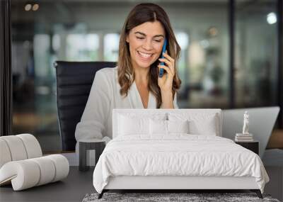 Happy smiling mature middle aged business woman, 40s professional lady executive manager talking on the phone making business call on cellphone at work in office using laptop computer. Wall mural