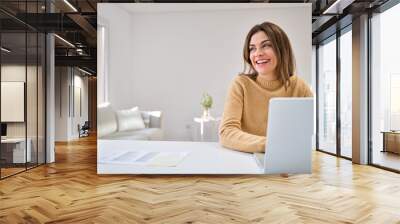 Happy smiling older mature middle aged woman using laptop computer sitting at table in living room, hybrid working, elearning online with technology device at home, looking away at copy space. Wall mural