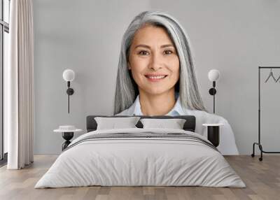 Happy smiling stylish confident 50 years old Asian female professional standing looking at camera at gray background. Portrait of sophisticated grey hair woman advertising products and services. Wall mural