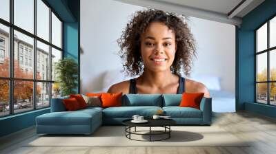 Happy smiling young attractive African American mixed race girl in sportswear posing indoors at modern bedroom apartment house looking at camera. Headshot close up portrait. Wall mural